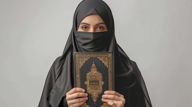 Happy Saudi Muslim woman wearing a black chador and holding a copy of the Holy Quran, isolated on white in a portrait