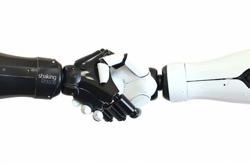 Two robots shaking hands. The robots are white and black. The robots are made to look like humans
