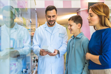 Cheerful pharmacist chemist man giving vitamins to young mom with son in the modern pharmacy.