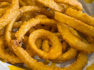 Macro of golden, fried onion rings in white wax paper lined basket
