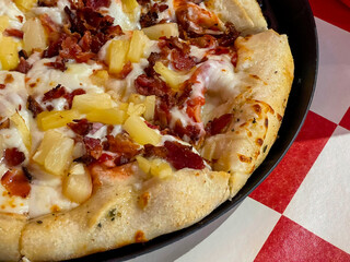 Closeup of Hawaiian pizza on red and white checkered table cloth