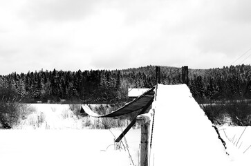 Lviv Oblast / Ukraine: Wintry impression of a small snow covered simple suspension bridge over the...