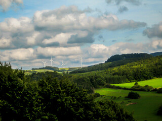Fototapeta na wymiar The low forest covered hills and open farmlands of the Eifel Region in Germany on a sunny day, with wind turbines in the background