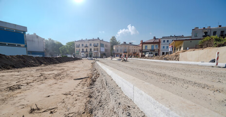 Budowa dróg w Ostrowcu pod błękitnym niebem w południe we wrześniu. Granitowe krawężniki na drodze  w budowie. Chaos budowlany w centrum miasta.