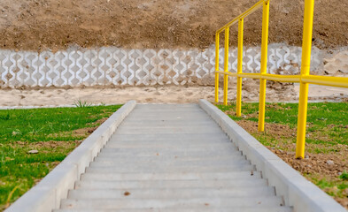 Świeżo zbudowane betonowe schody z żółtą stalową poręczą. Betonowe schody prowadzące w dół zbocza na skraju nowo wybudowanej drogi. - obrazy, fototapety, plakaty