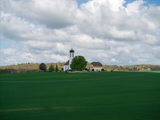 Small church with cemetery in the middle of blooming fruit trees and fields captured with a drone in spring
