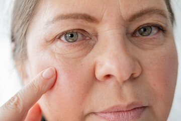 close up mature female face, aging woman 55 years old gazes herself in mirror, wrinkles,...