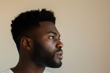 Obraz premium Side view of a young man sporting a modern fade hairstyle with meticulous facial hair against a neutral background