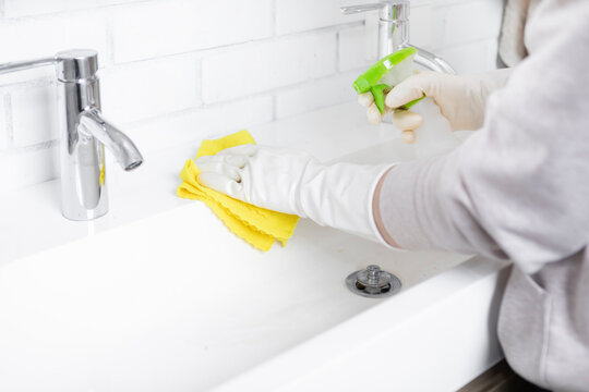 Close-up shot of woman in rubber gloves cleans sink and faucet with a rag and spray in the bathroom. Household and cleaning concept