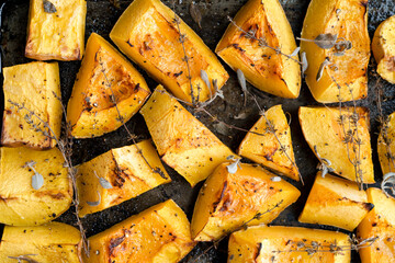 Pieces of organic oven roasted butternut squash in a baking sheet pan with fresh thyme and sage herbs in natural light.
