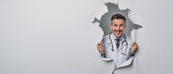 Charming male doctor giving thumbs up while peeking through a white paper tear