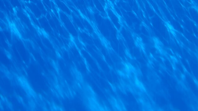 Pure transparent blue water in the swimming pool with diagonal light reflections. 4k resolution video of texture of water in swimming pool.
