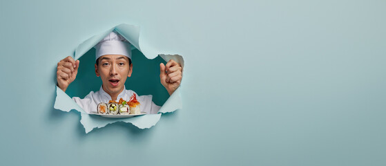 Energetic chef with sushi plate tearing through a blue paper backdrop, showing vibrancy