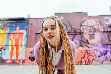 Stylish hipster girl with braids hairstyle having fun leaned toward the camera against colorful graffiti wall.