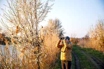 Bird watching. Woman ornithologist with binoculars observes birds arriving at lake in spring