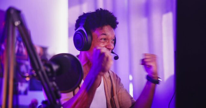 Gaming, winning and man with headphones, live stream and success for esports, neon or achievement. Gamer, influencer or streamer with mic for online broadcast, celebration and content creator in home