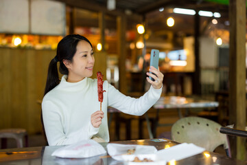 Woman use mobile phone to take selfie with Taiwanese sausage at market