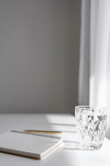 Minimalist white and grey aesthetic background with journal or notebook and glass of water, morning routine and studying theme