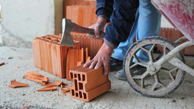 The rugged work at a construction site as a worker trims bricks using an axe, chipping off pieces with precision and skill.