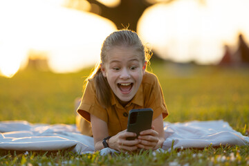 Child girl playing online video game with her friend on cellphone outdoors in summer park