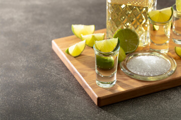 Tequila with sea salt and lime slices on a cutting board.