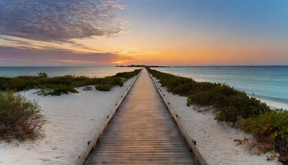Naklejka premium boardwalk leading to the white sand beach and ocean water at sunset with few shrubs on sides