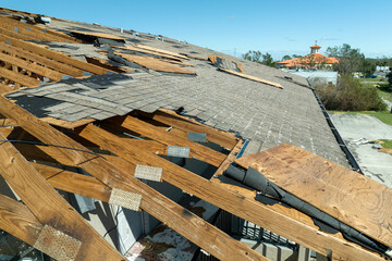 Ruined rooftop in need of repair. Wind damaged house roof with missing asphalt shingles after...