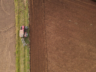 Aerial view of a red tractor plow the farmland 