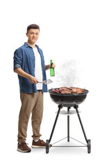 Young man making a barbecue and holding a bottle of beer - obrazy, fototapety, plakaty