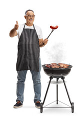 Mature man baking meat on a barbecue grill and holding a sausage with a fork