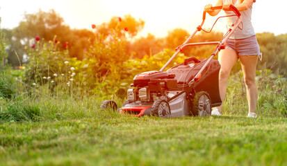 girl with a lawnmower mows the green lawn - obrazy, fototapety, plakaty