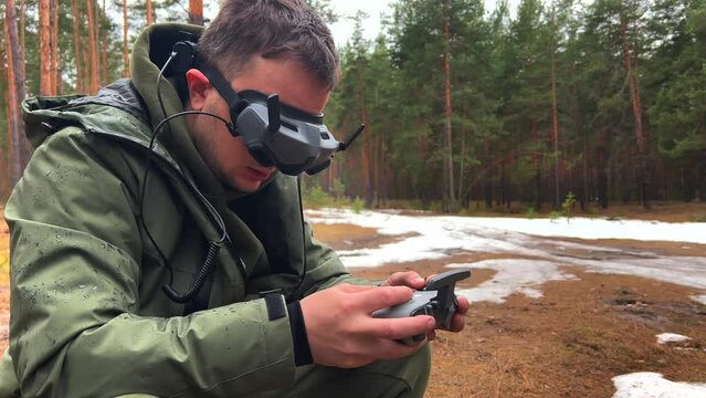 A young man in camouflage clothes flies a quadcopter in a pine forest