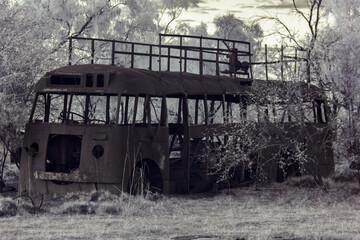 Side view of an abandoned, rusted tour bus in a forest, capture in infrared