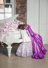 Young beautiful sad crying woman in fantasy rococo style medieval dress sitting near piano