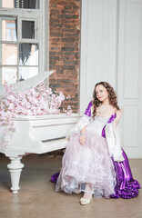 Young beautiful flirtatious woman in fantasy rococo style medieval dress sitting near piano with...