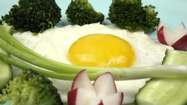 Fried egg, boiled broccoli, radishes, fresh cucumbers and green onion are on a pale blue plate, healthy breakfast             