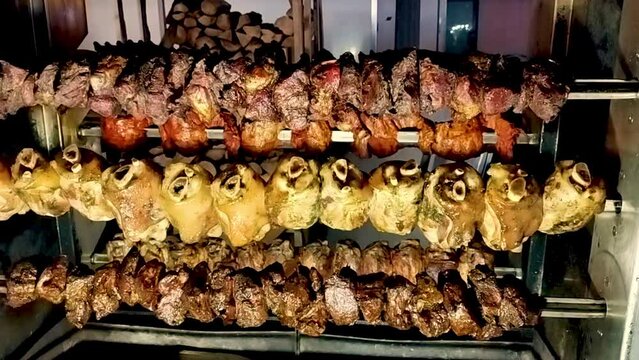 Grill with rotating skewers and drawer with embers: on different levels we see skewers of pork ribs, shanks and sausages rotating. You can see some smoke rising. Italian food and traditions.
