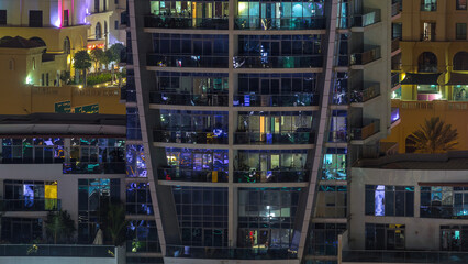 Rows of glowing windows with people in apartment building at night.