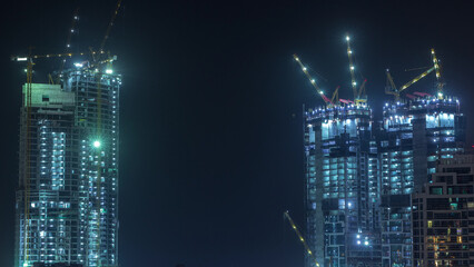 Aerial view of a skyscraper under construction with huge cranes timelapse in Dubai marina.