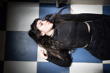 Beautiful girl with a gothic look, dressed in black clothes, lying on the floor. Attractive woman with closed eyes for fashion concept