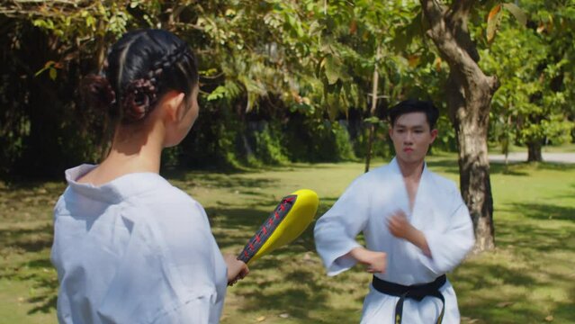 Medium shot of male taekwondo fighter performing kicks with female partner in park