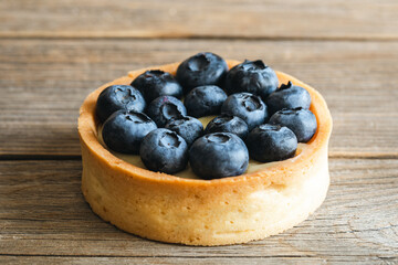 Homemade mini tart with blueberries and whipped cream on a wooden background, close up.