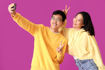 Young Asian friends taking selfie on violet background