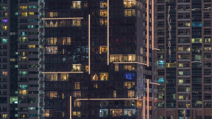 Fototapeta na wymiar Rows of glowing windows with people in apartment building at night.