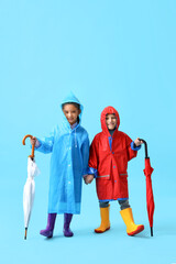 Little children in raincoats and rubber boots with umbrellas on blue background