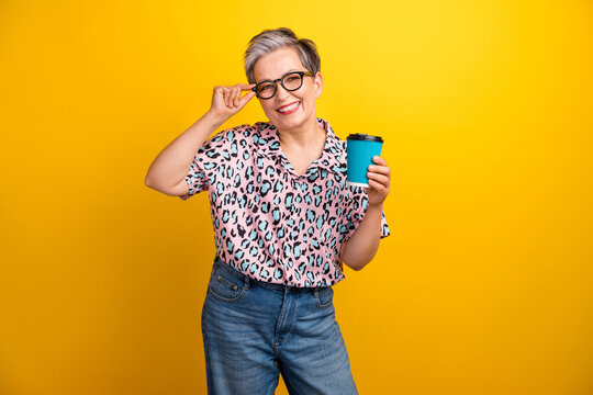 Photo portrait of lovely senior lady hold coffee paper cup drink dressed stylish leopard print garment isolated on yellow color background