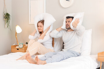 Young couple with pillows suffering from loud neighbours in bedroom