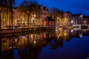 Fototapeta na wymiar Lier city in Belgium at night. warm lights reflect on water at evening people eat and drink in street of old houses historic building Buyldragershuisje. nightlife on Feix timmermansplein square