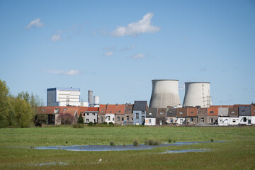 cooling tower chimneys from Vilvoorde industrial power plant outside Brussels Belgium above rooftops of residential skyline and green field area for public recreation on sunny blue sky day - 781545253