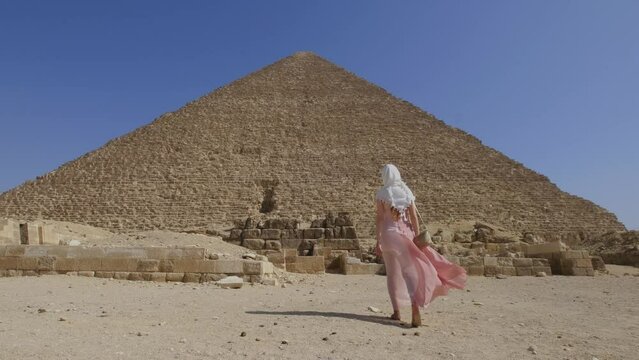 Back view of the young woman walking towards the Great Pyramids of Giza in Egypt. Tourist travel concept.